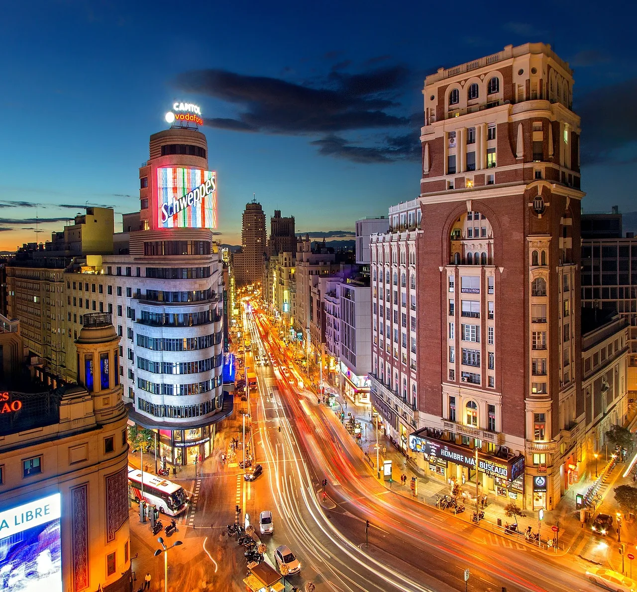 Calle Gran Vía en Madrid de noche, con el letrero de Schweppes del Edificio Capitol y estelas de luz de vehículos.