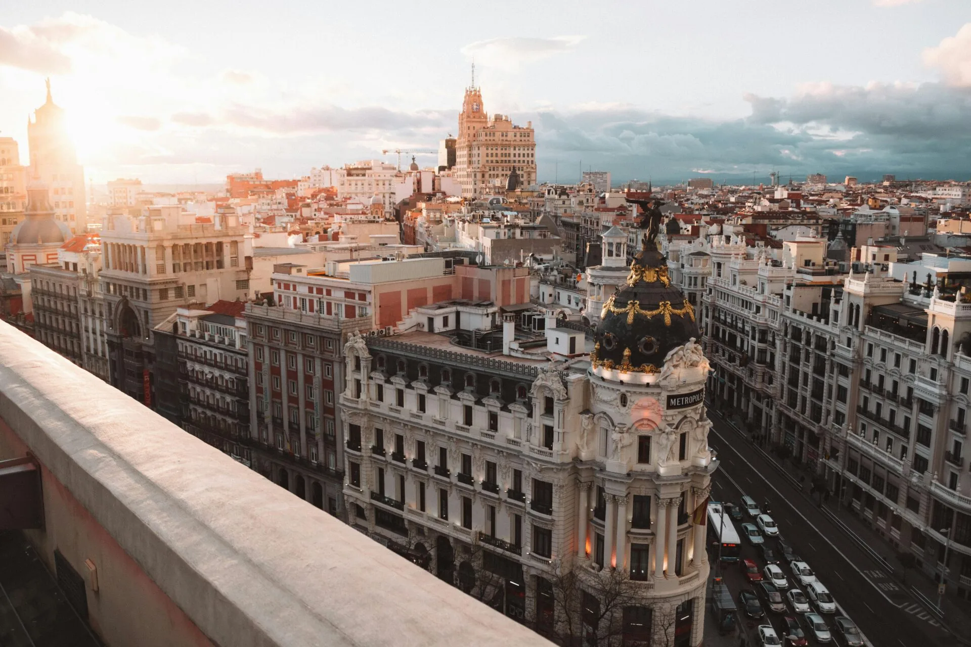 Vista aérea de la Gran Vía de Madrid al atardecer, con el Edificio Metrópolis y un panorama de tejados urbanos bajo un cielo