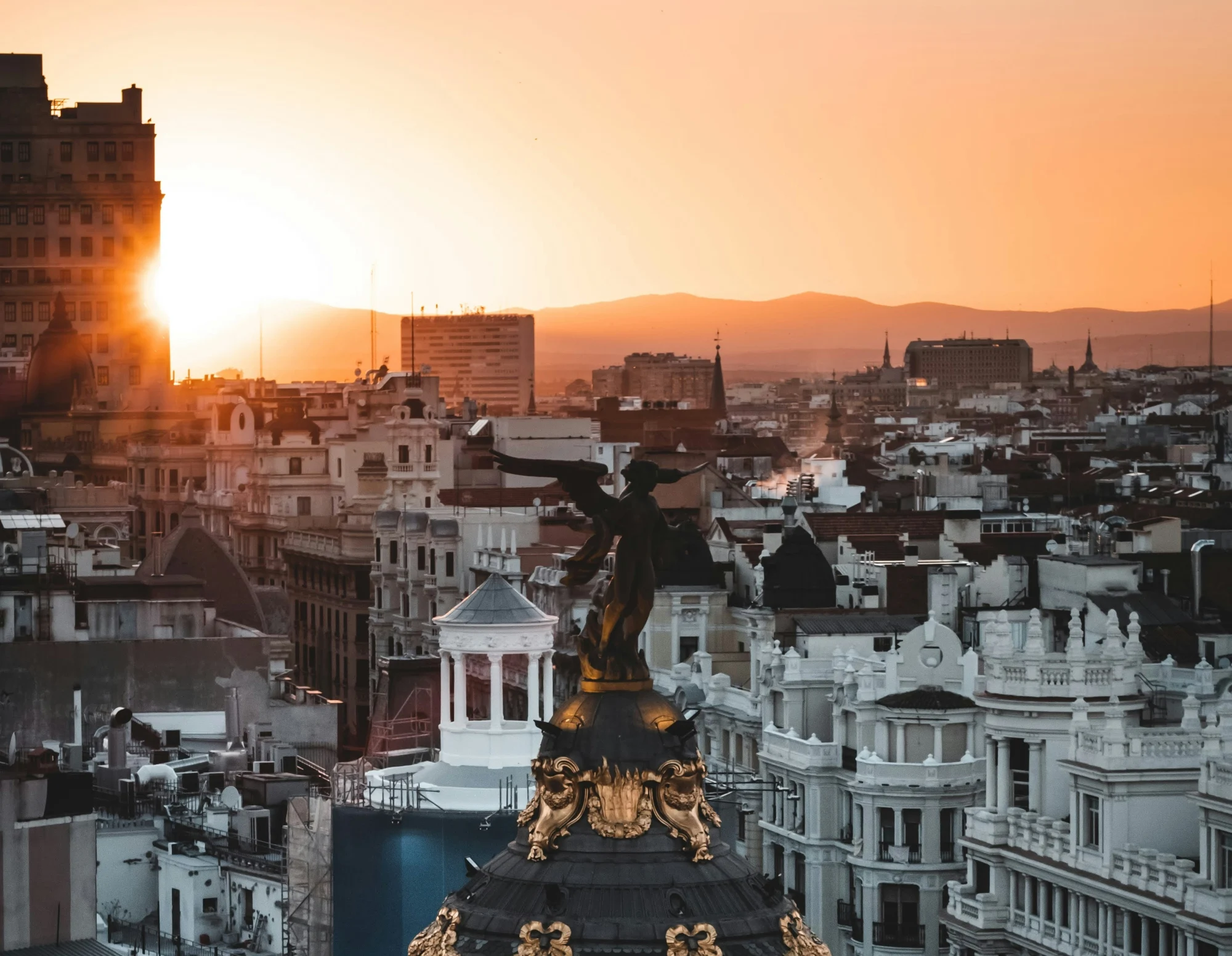 Tejados de Madrid al atardecer, con la cúpula del Edificio Metrópolis y una estatua de la Victoria Alada en primer plano.