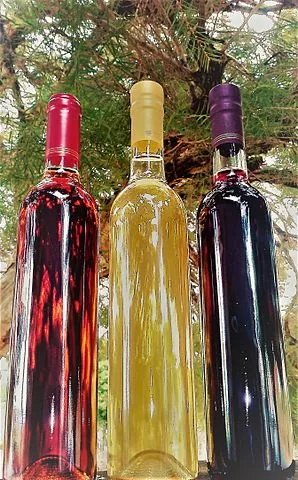 Tres botellas de hidromiel con líquidos rojos, dorados y rojo oscuro, de pie sobre un fondo verde borroso.