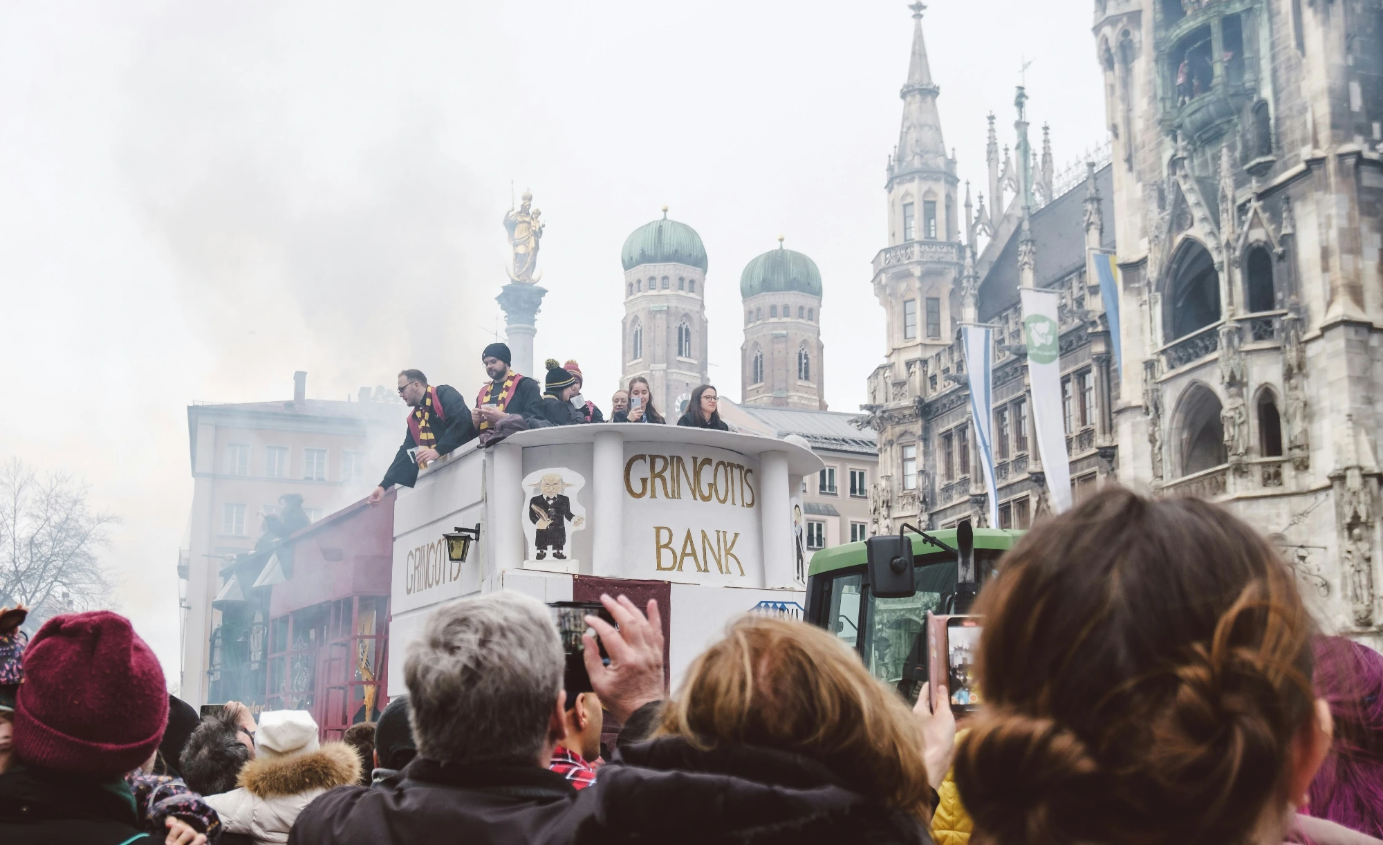 A Gringotts Bank float with costumed people on top moves through Marienplatz in Munich during a parade. Frauenkirche towers a