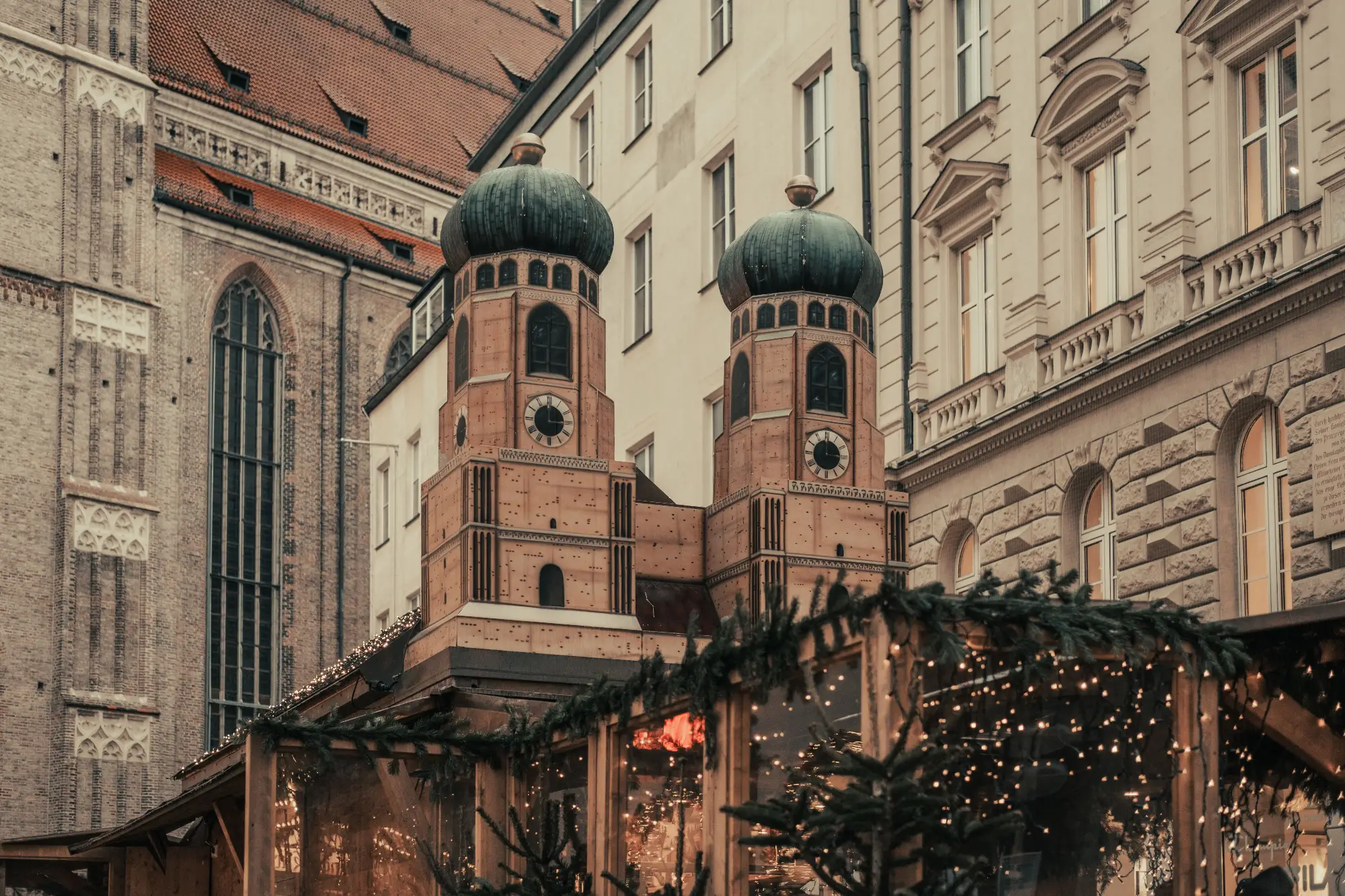 Drewniane stoisko jarmarku bożonarodzeniowego z miniaturą wież Frauenkirche na tle kamienic w Monachium.