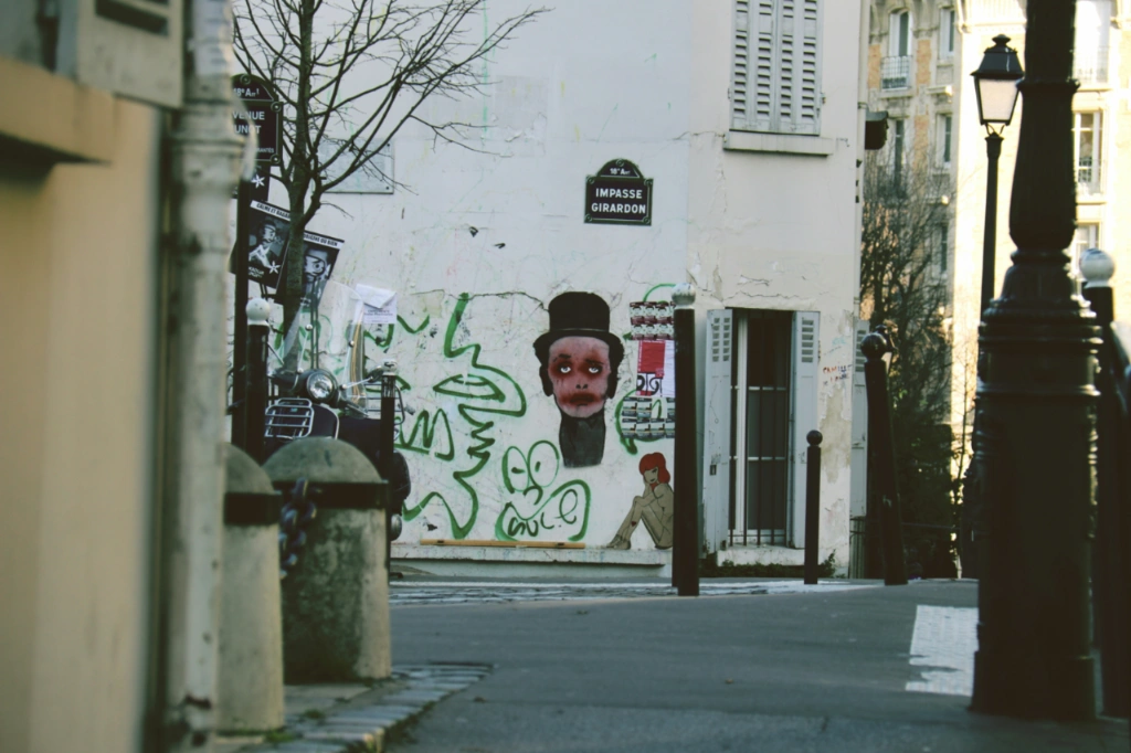 Street scene in Paris with a white building covered in green graffiti and a distinctive figure in a top hat. A street sign re