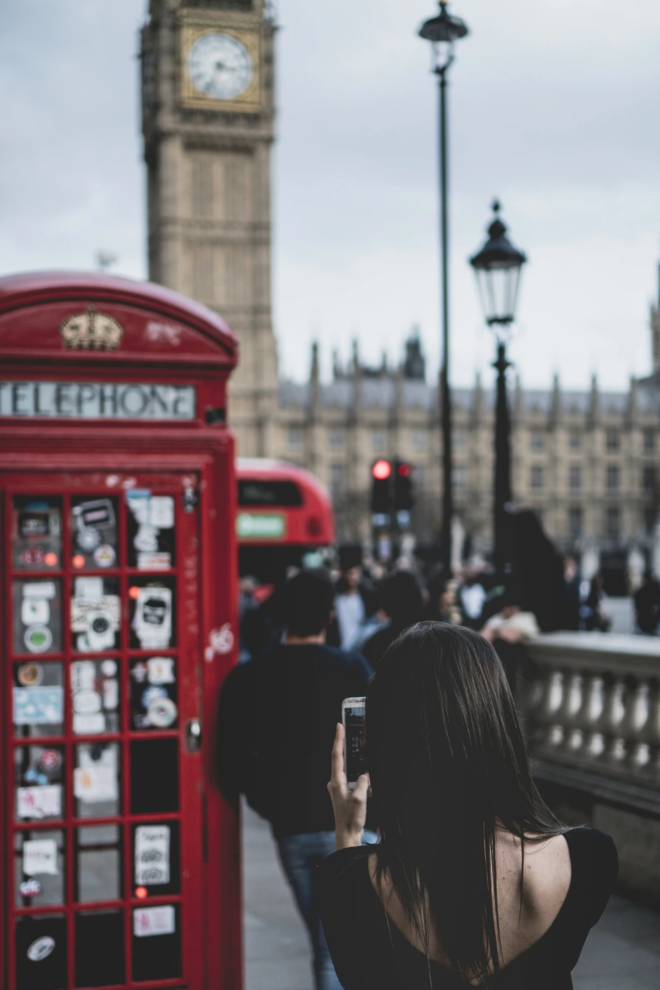 Kobieta fotografuje czerwoną budkę telefoniczną, z rozmytą w tle Wieżą Elżbiety (Big Ben) i budynkiem Parlamentu.