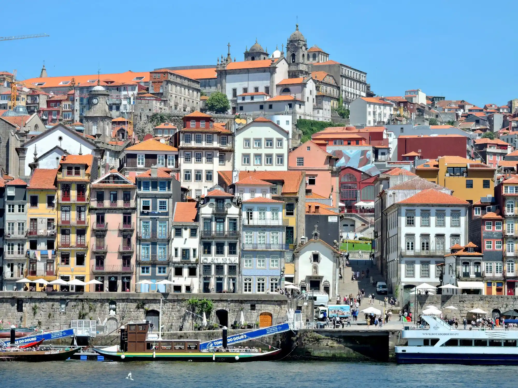 Colorful historic buildings of Porto's Ribeira district rise above the Douro River, with tour boats moored at the waterfront.