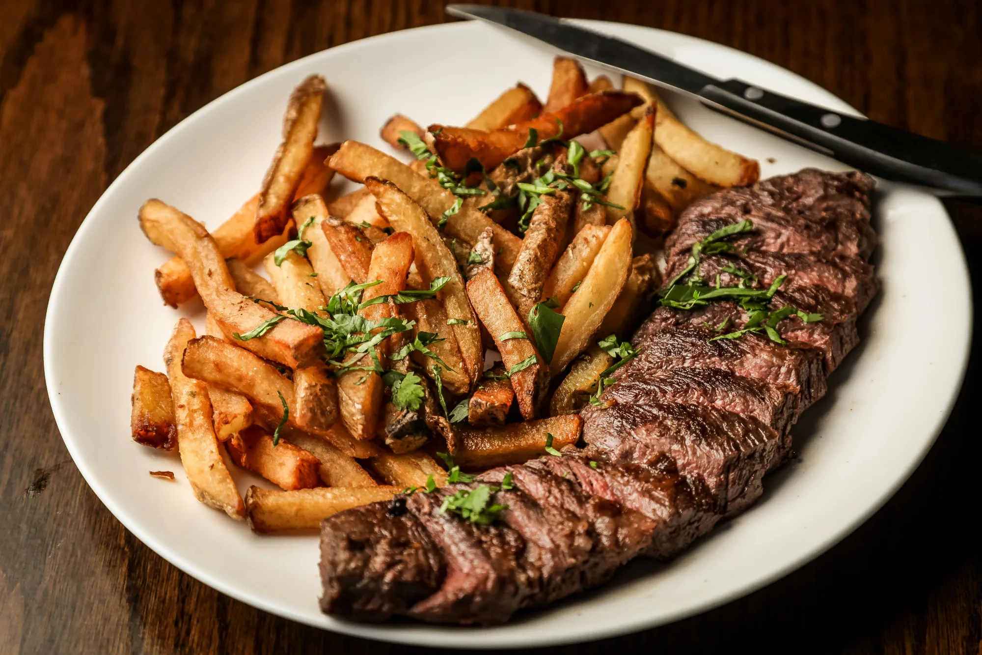 Un plato de steak frites, con un filete a la parrilla en rodajas junto a un montón de patatas fritas con hierbas frescas.