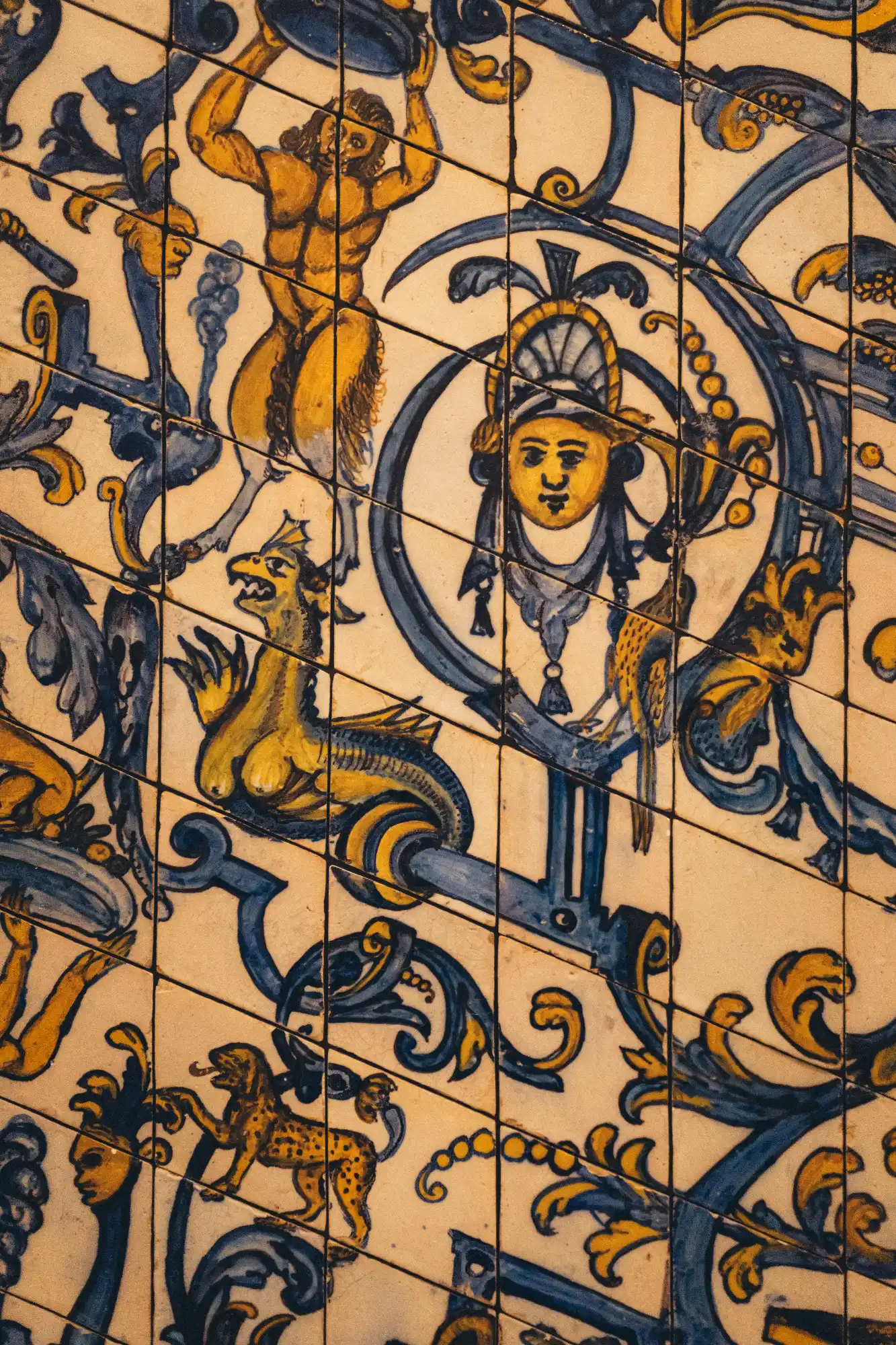Zbliżenie na żółto-niebieskie płytki ceramiczne z postaciami mitologicznymi, w tym satyrem, smokiem i lampartem.