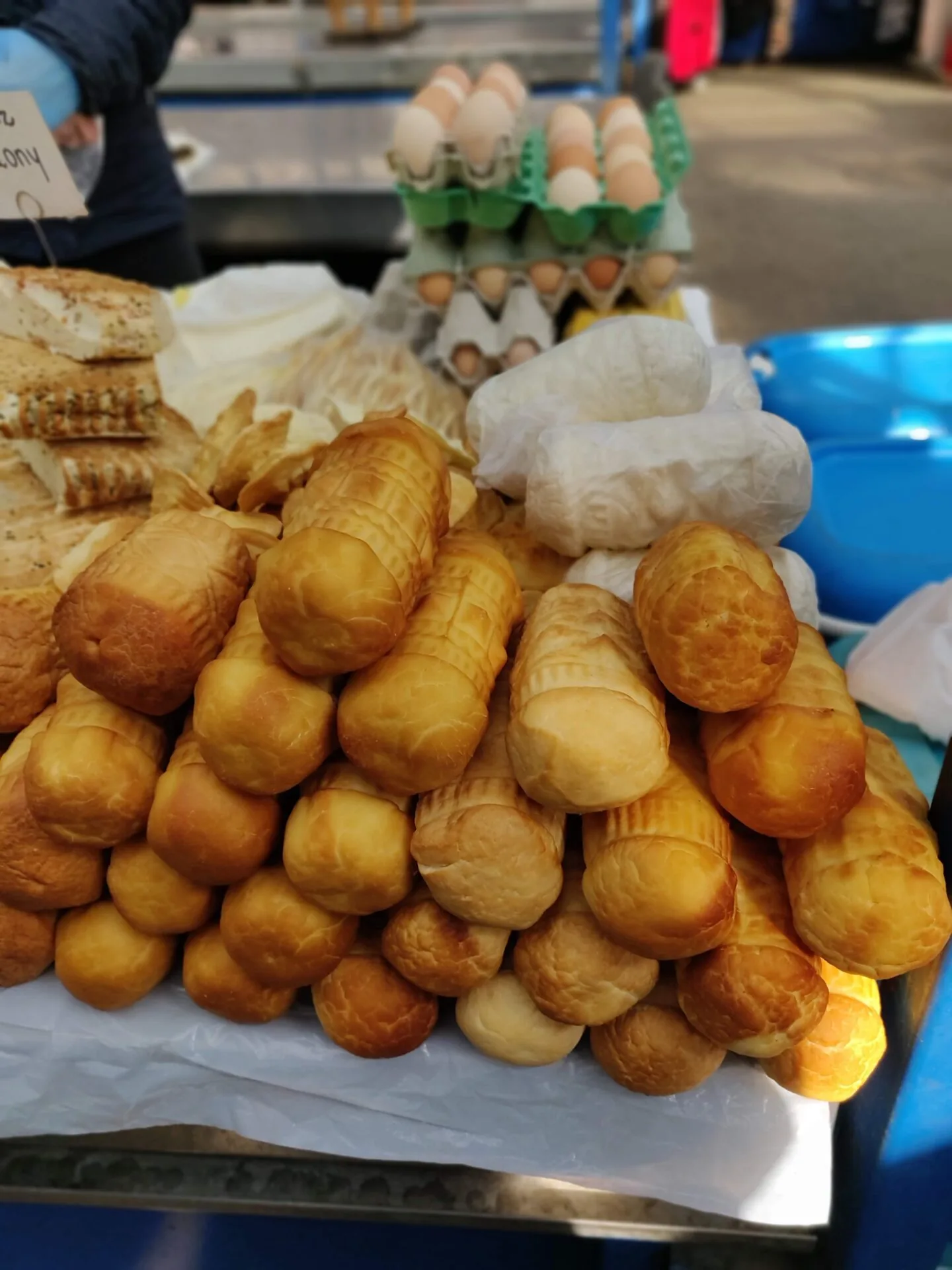 A stall at a market with a large pile of golden-brown smoked oscypek cheese, fresh eggs in cartons, and other baked goods.