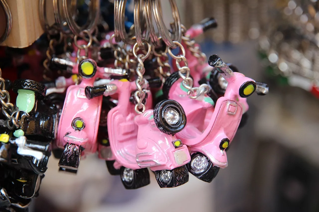 Close-up of numerous small pink scooter keychains hanging from metal rings, with other dark keychains partially visible.