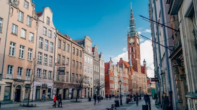 Histórica calle Długi Targ en Gdańsk con coloridas casas mercantes y la torre del Ayuntamiento Principal bajo un cielo azul.
