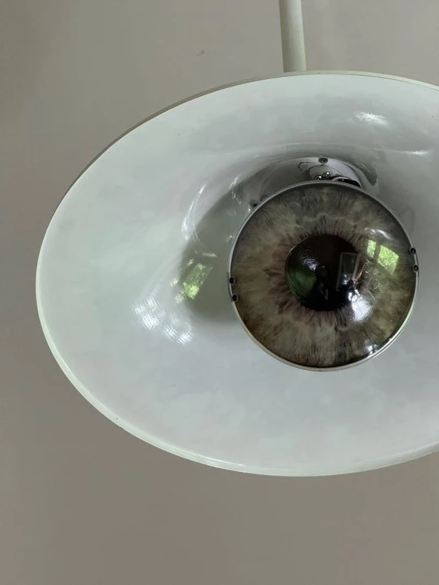 Close-up of a white ceiling lamp where the lightbulb is designed to look like a realistic human eye.
