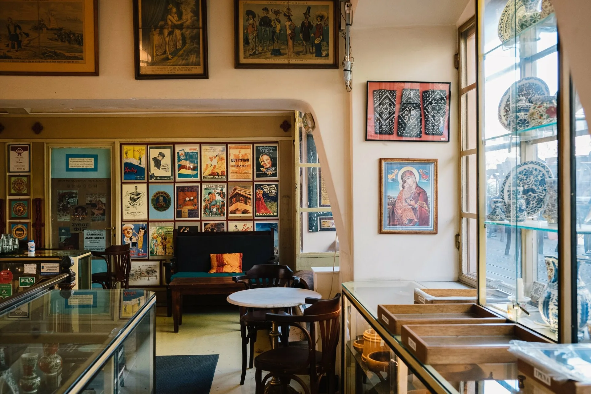 Vintage interior of a traditional Greek cafe with wooden chairs, marble table, glass display cases, and framed posters.