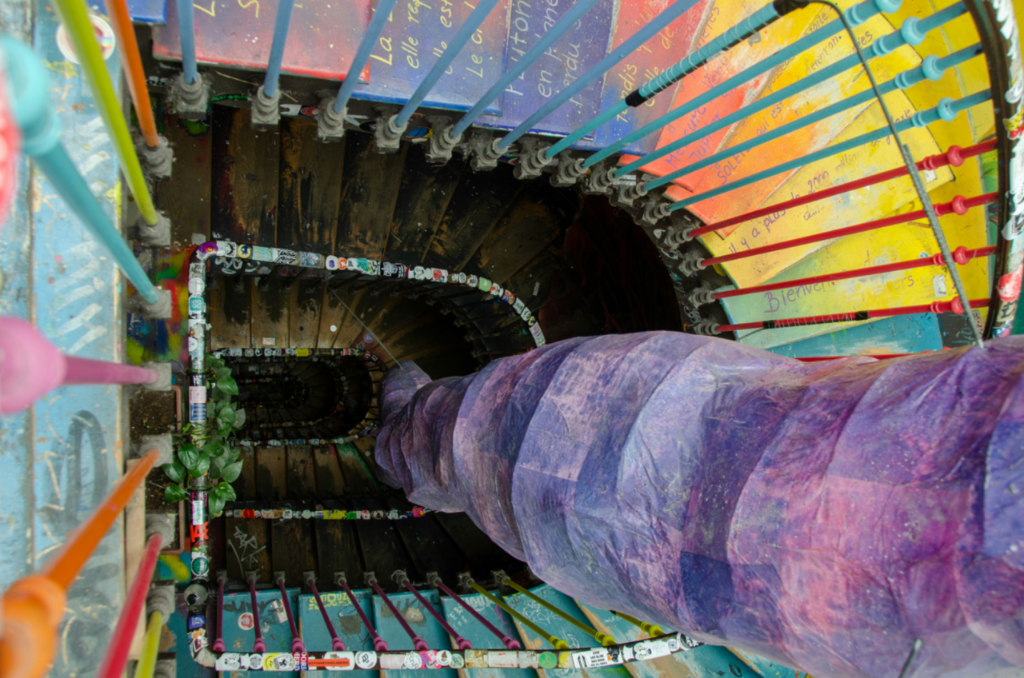 The artistic spiral staircase inside the 59 Rivoli art squat in Paris, decorated with murals and stickers. Top-down view of the colorful spiral staircase at 59 Rivoli, featuring rainbow railings and painted steps.