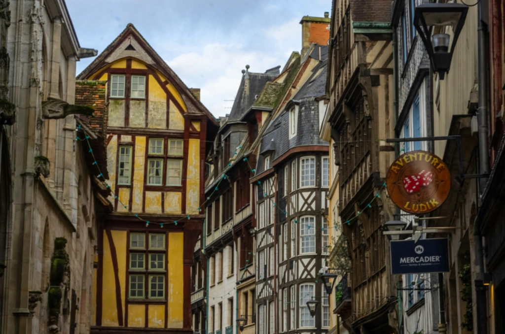 Narrow historic street with traditional half-timbered houses and stone gargoyles.