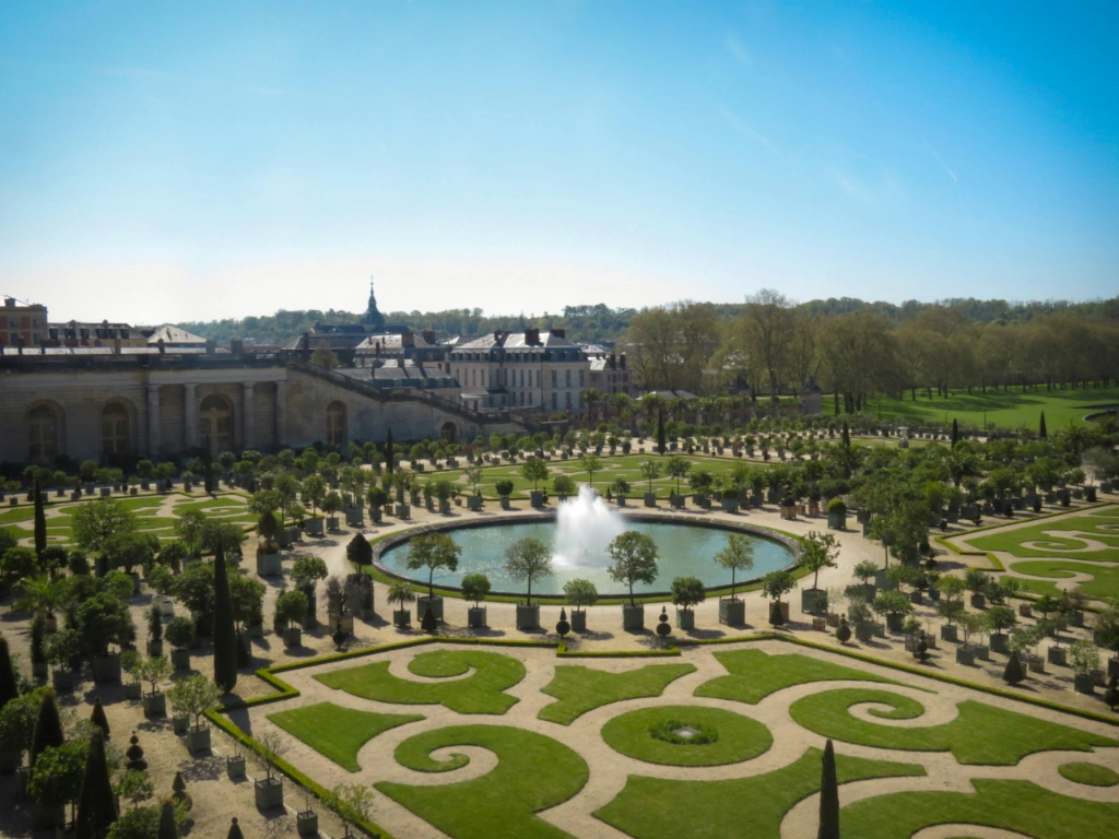 View of the formal Orangerie gardens and fountain at the Palace of Versailles on a sunny day.