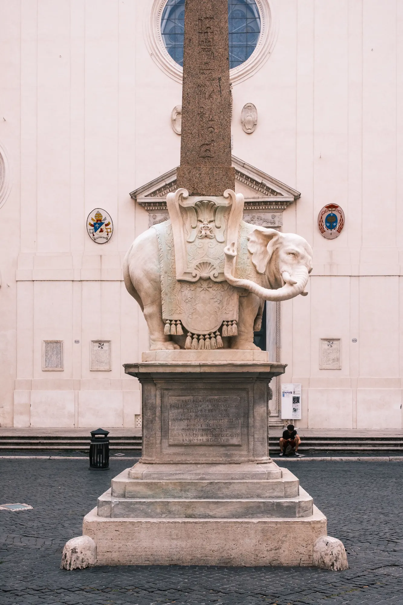 Marble elephant sculpture carrying an Egyptian obelisk on a stone pedestal in front of a church in Rome.