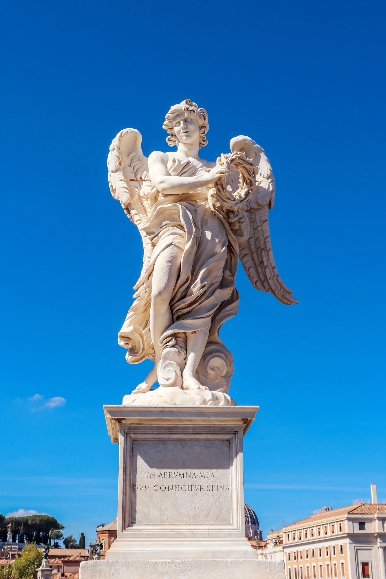 Marble statue of an angel holding the Crown of Thorns on a pedestal against a clear blue sky in Rome.