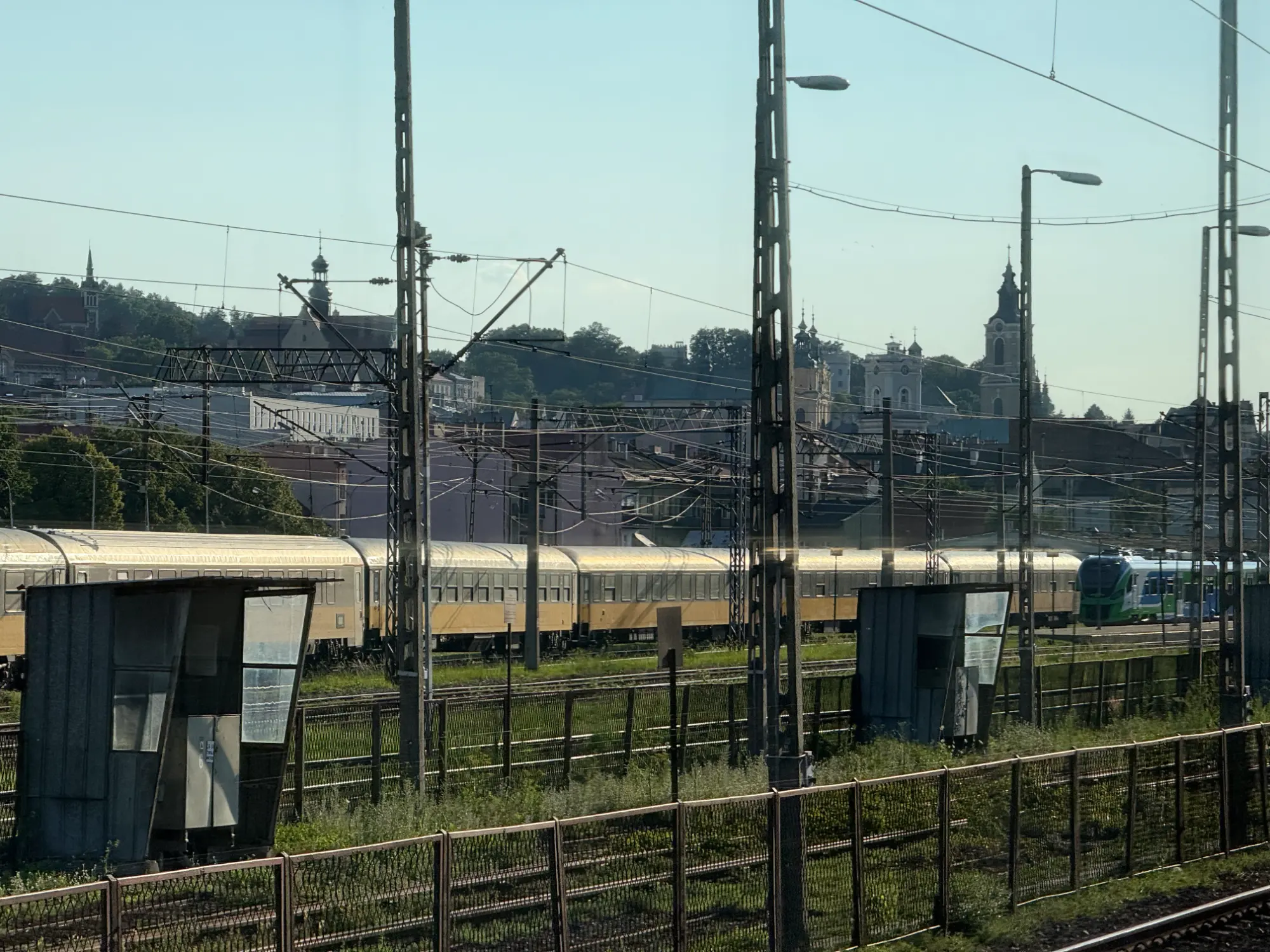 A passenger train passes the Przemyśl Główny railway tracks with historical church spires in the background.