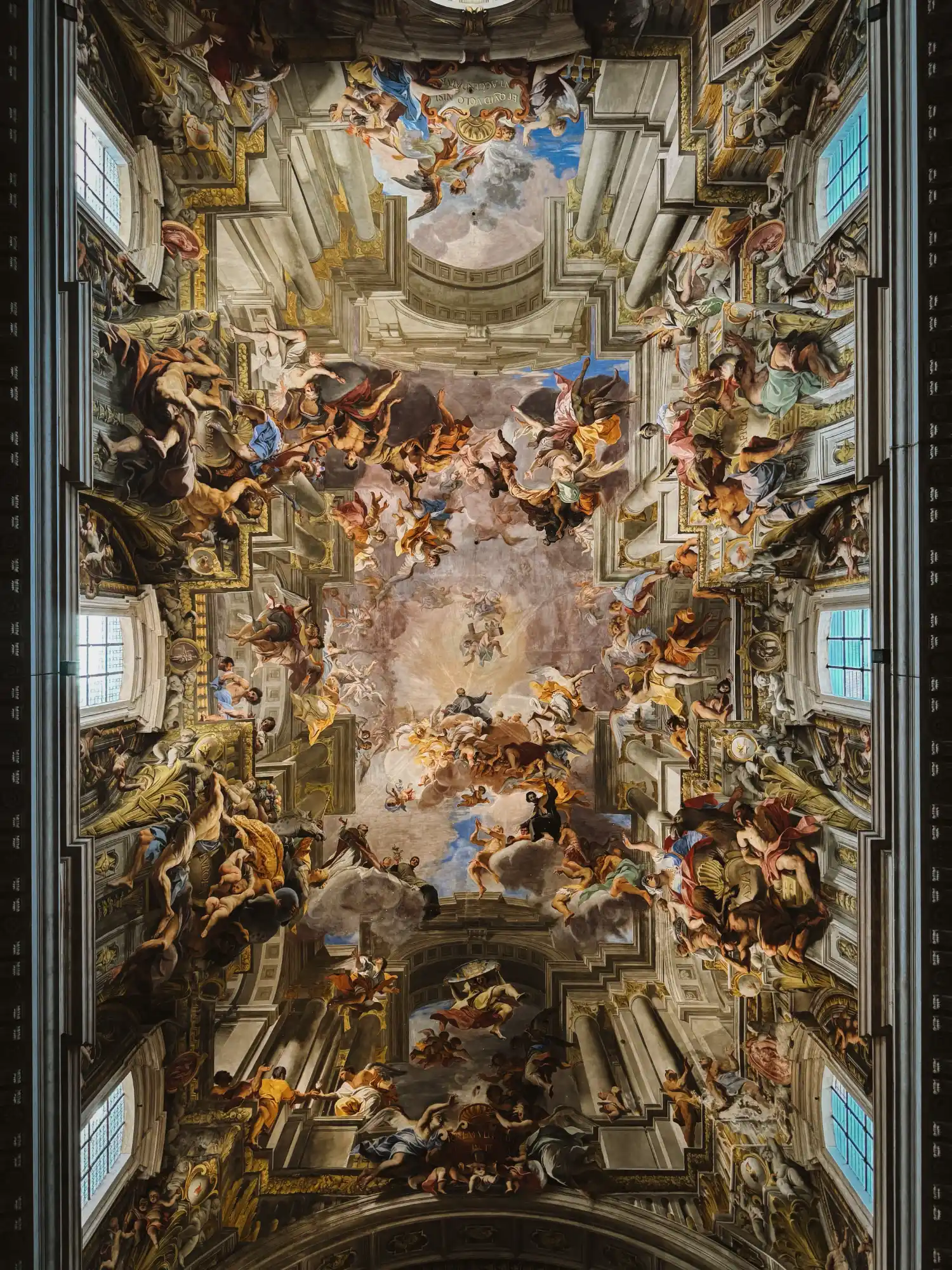 A worm's-eye view of the ornate, colourful Baroque fresco covering the entire barrel-vaulted ceiling of a grand Roman church.