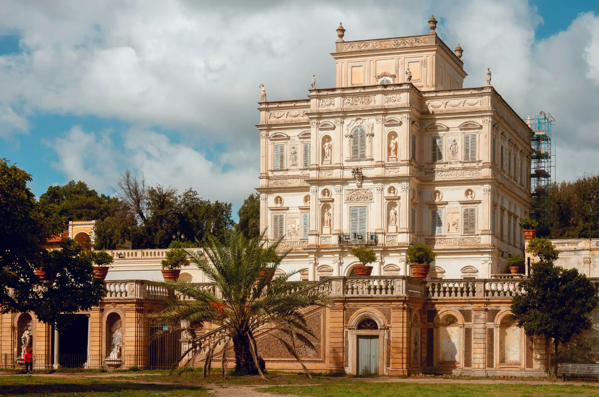 The ornate facade of the Casino del Bel Respiro in Rome's Villa Doria Pamphili park, with statues, and a palm tree.