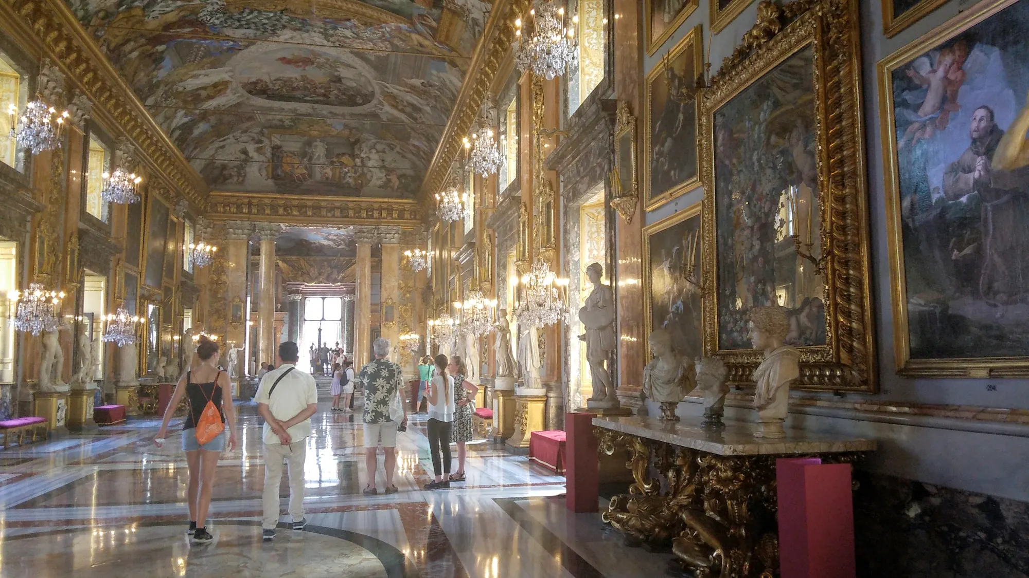 Tourists inside the opulent Great Hall of the Colonna Gallery, with its frescoed ceiling and gilded walls.