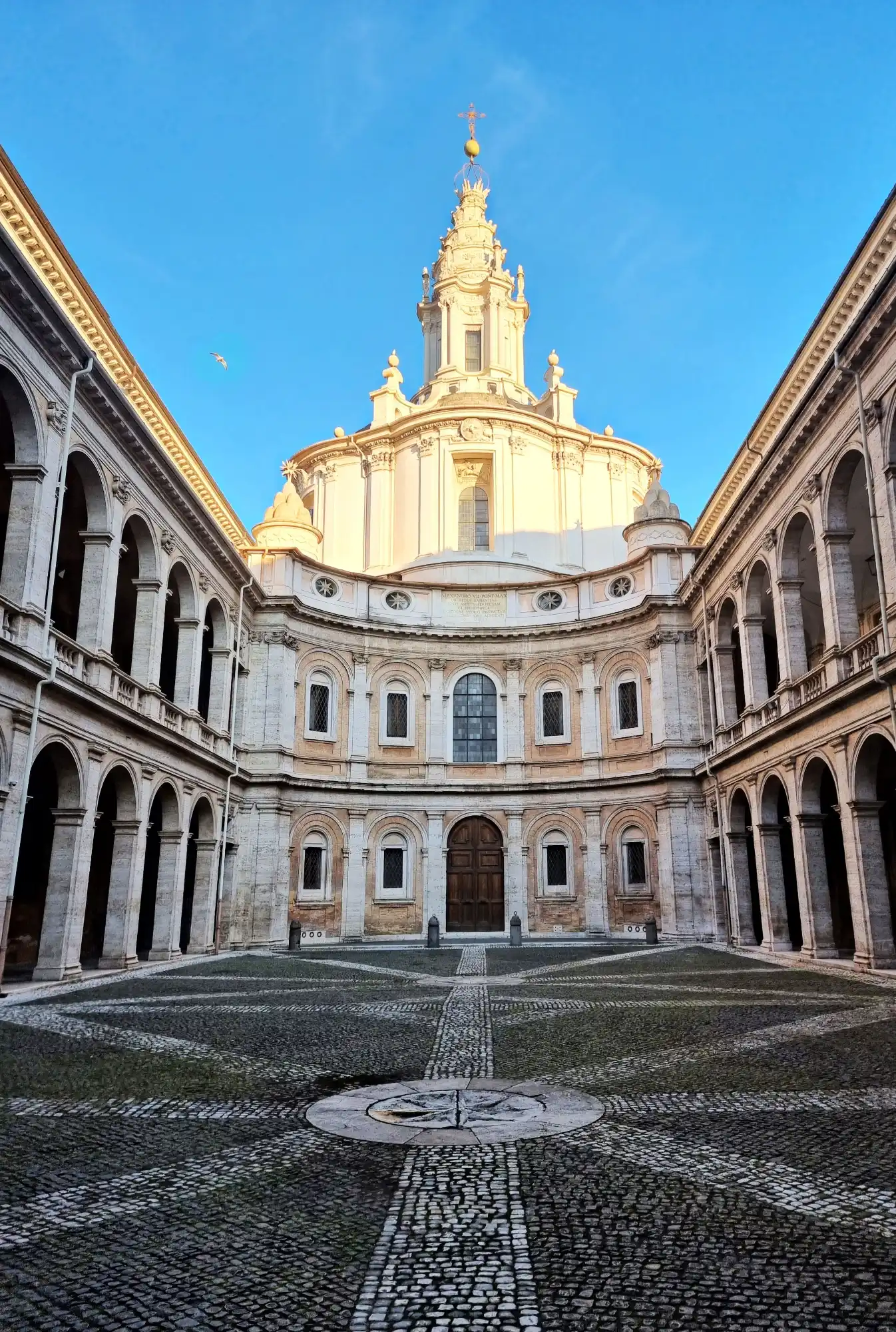 The courtyard of the Sant'Ivo alla Sapienza church in Rome, showing its concave baroque facade and cobblestone paving.