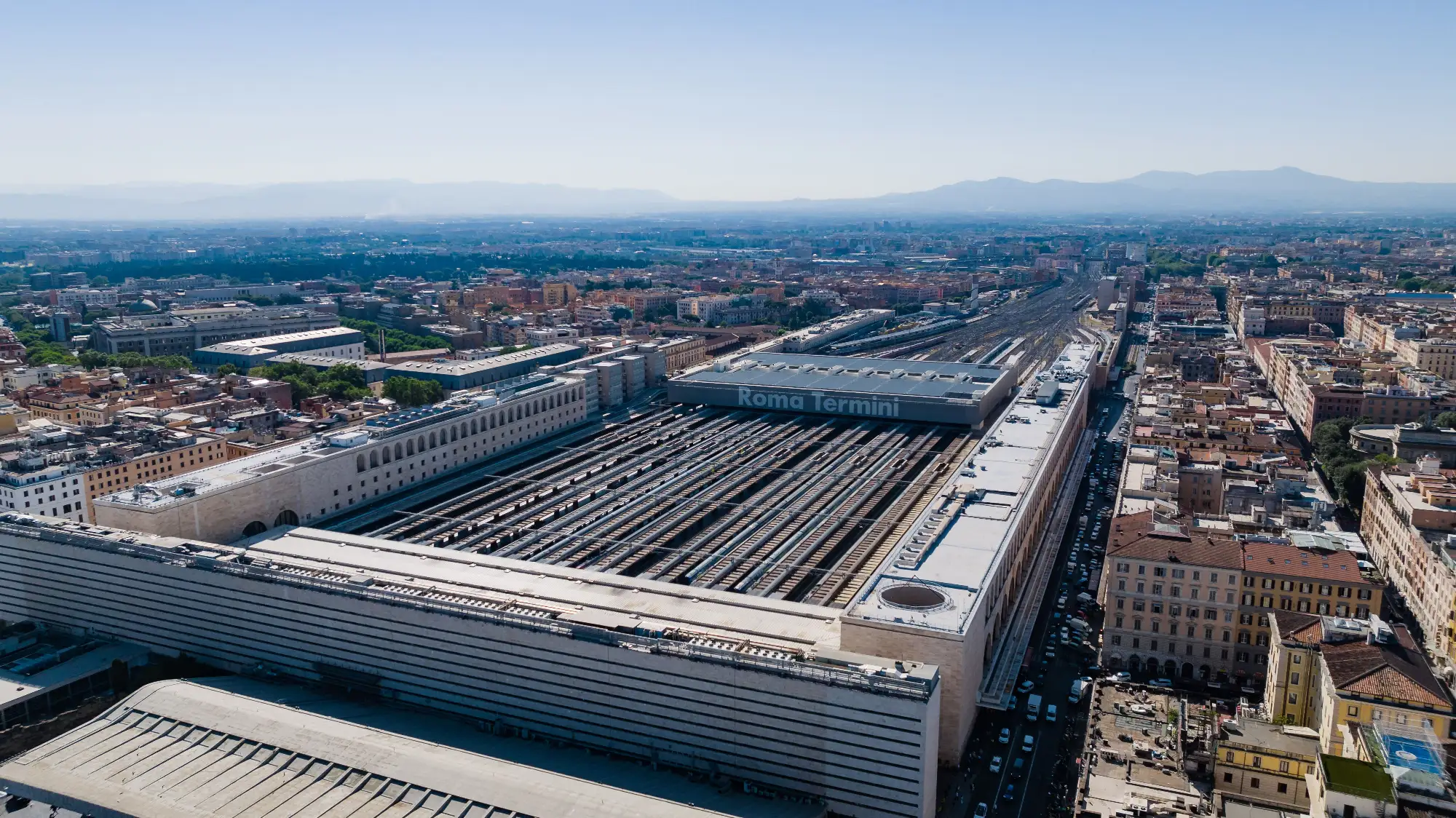 Aerial view of Roma Termini train station, with its many tracks spreading out into the city of Rome under a clear sky.
