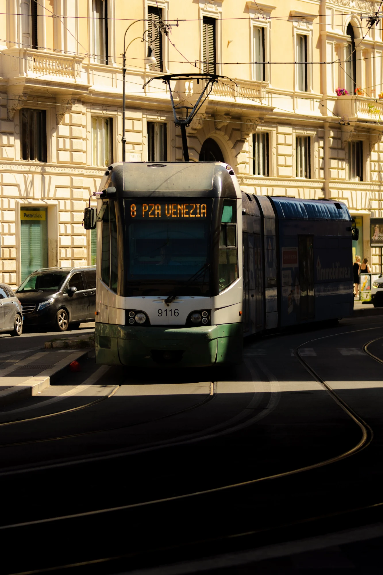 A modern tram on line 8 to Piazza Venezia in Rome turns a corner in the bright sunlight.