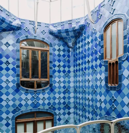 Interior courtyard of Casa Batlló with walls covered in blue, diamond-patterned tiles and wooden-framed windows.