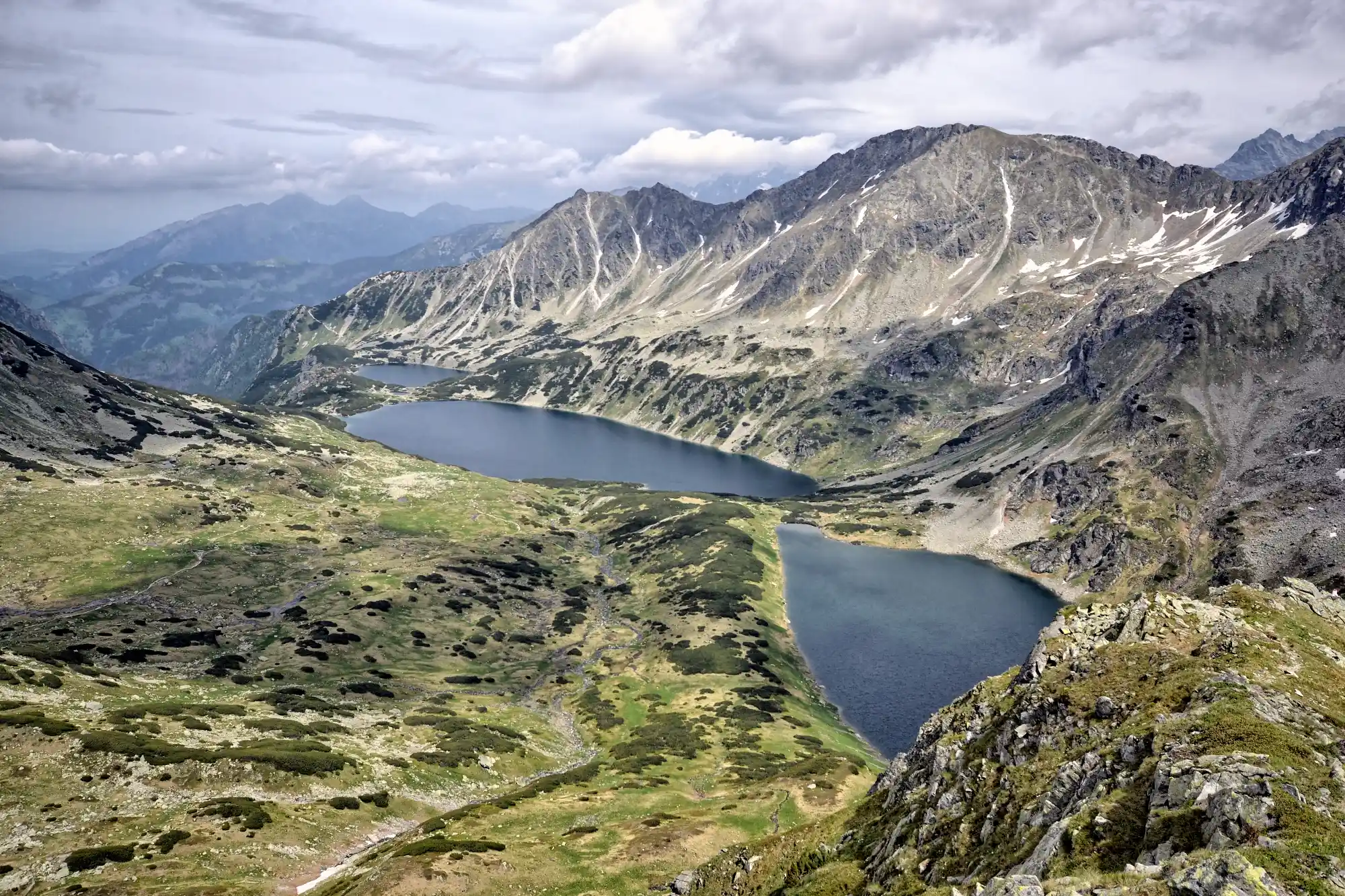 High-angle view over glacial lakes in a rugged mountain valley surrounded by rocky alpine peaks.