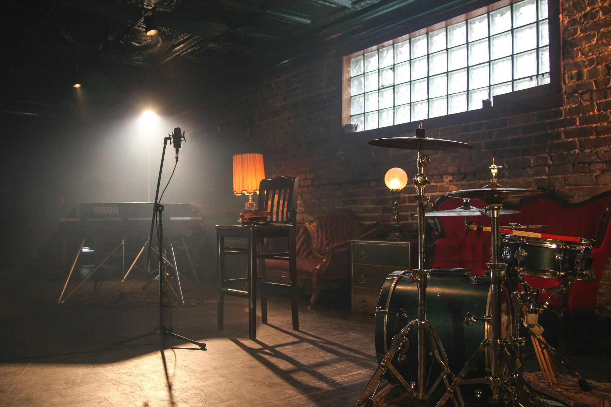 A dimly lit stage with a drum kit, microphone, and keyboard, set up for a live performance.