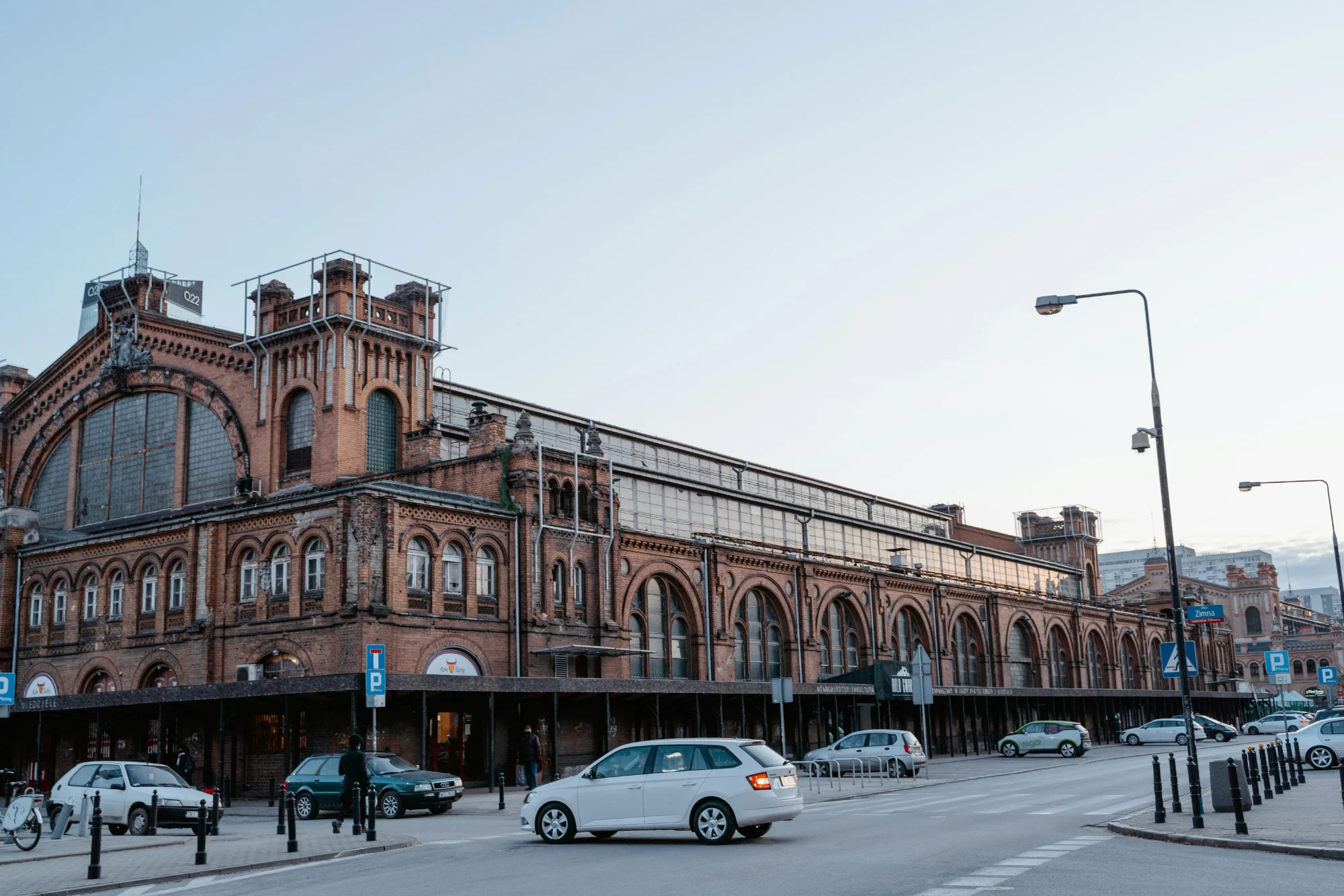 Exterior of the historic red-brick Hala Gwardii market hall in Warsaw with cars driving past.