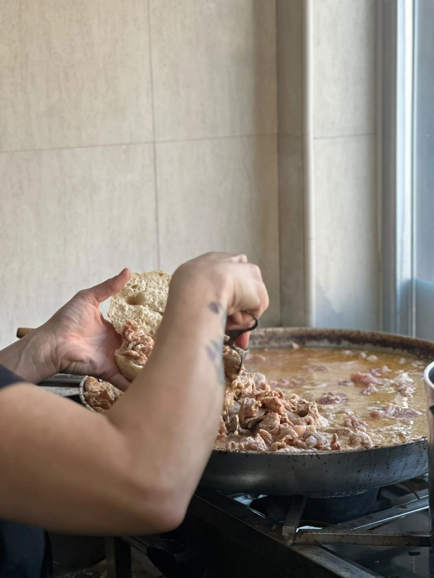 Cook filling a crusty bread roll with simmered pork slices from a large pan in Parreirinha do Chile.