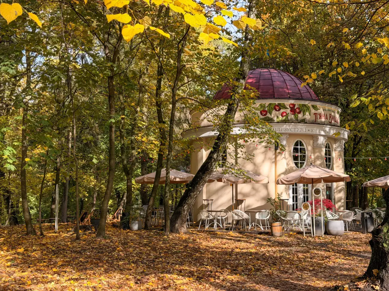 Round rotunda pavilion cafe with a domed roof and outdoor seating surrounded by autumn trees.