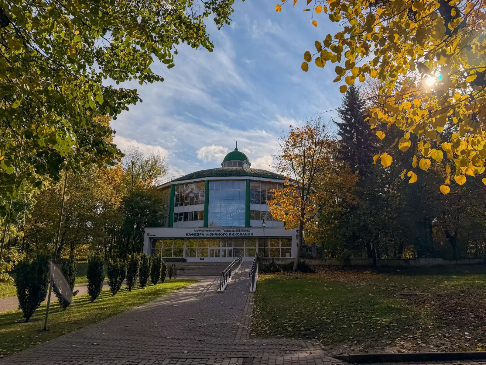 Round modernist building of Lviv Polytechnic surrounded by autumn trees and a paved path.