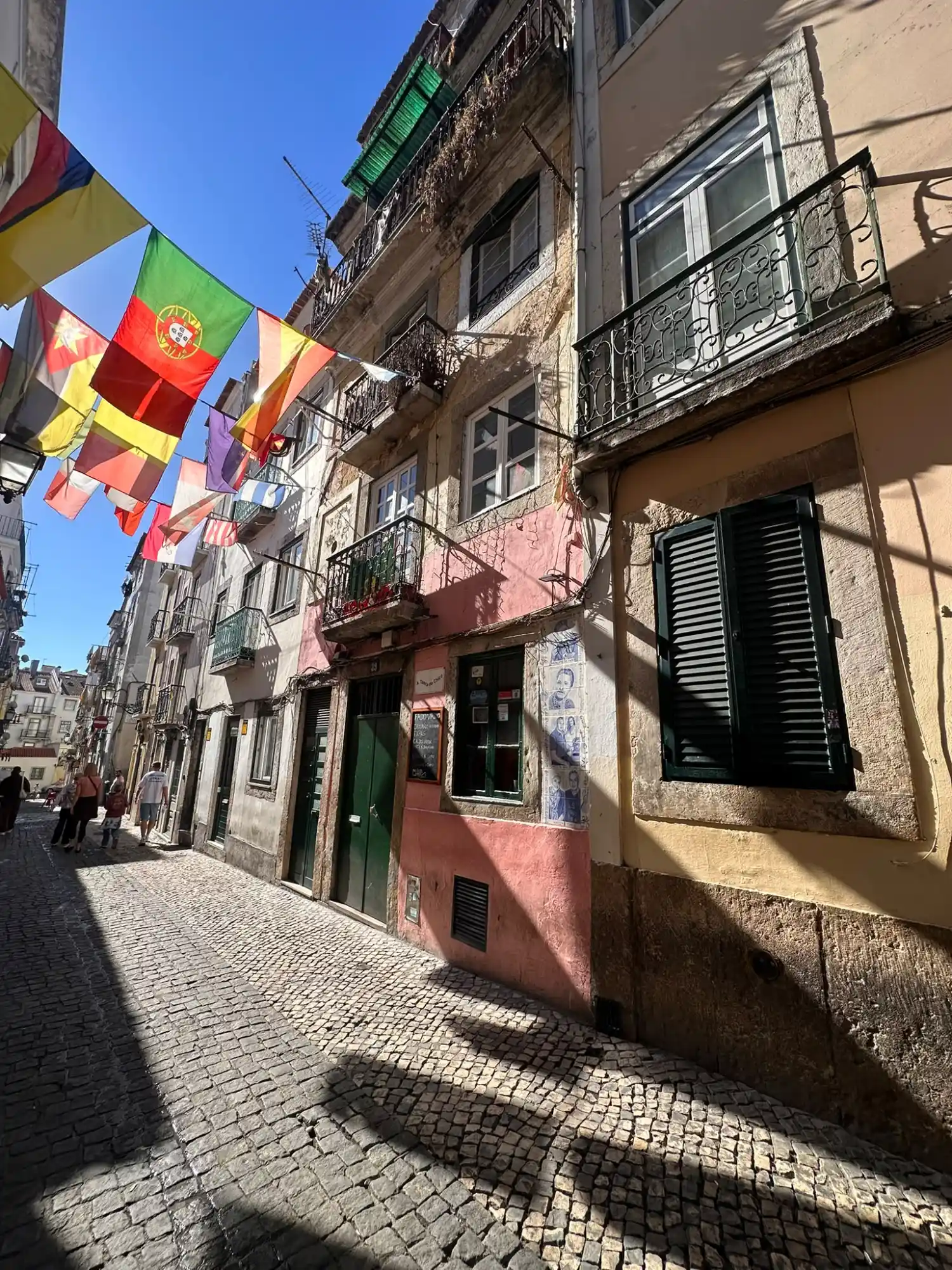 Narrow cobblestone street with colourful flags strung overhead between old residential buildings in Lisbon.