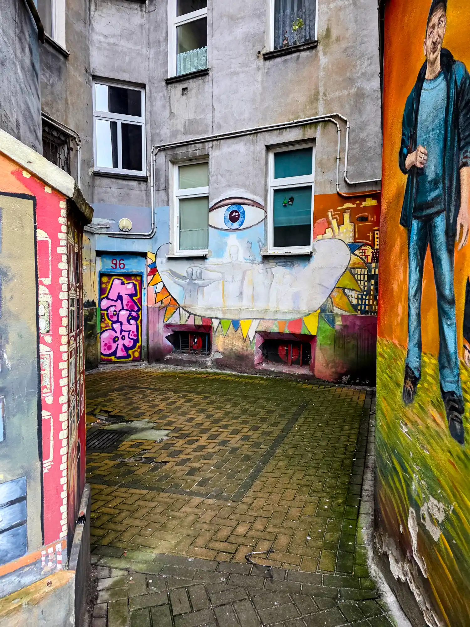 A narrow, paved courtyard in Wrocław's Nadodrze district, with its walls covered in colourful murals and street art.