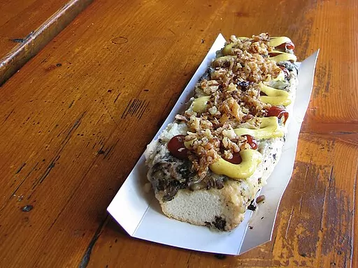 Open-faced zapiekanka sandwich with mushrooms, melted cheese, ketchup, mustard, and fried onions on a wooden table.