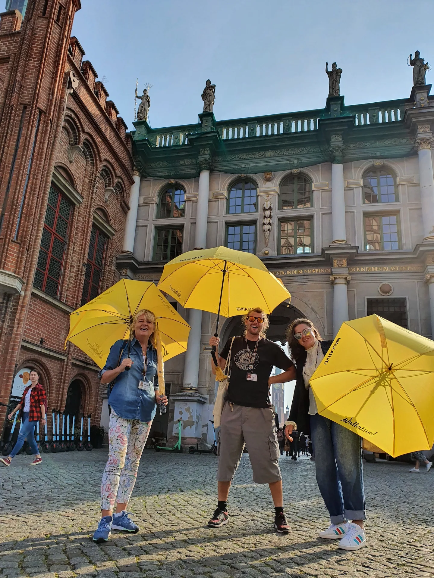 Weseli turyści na wycieczce z przewodnikiem w Gdańsku, przed Bramą Złotą.