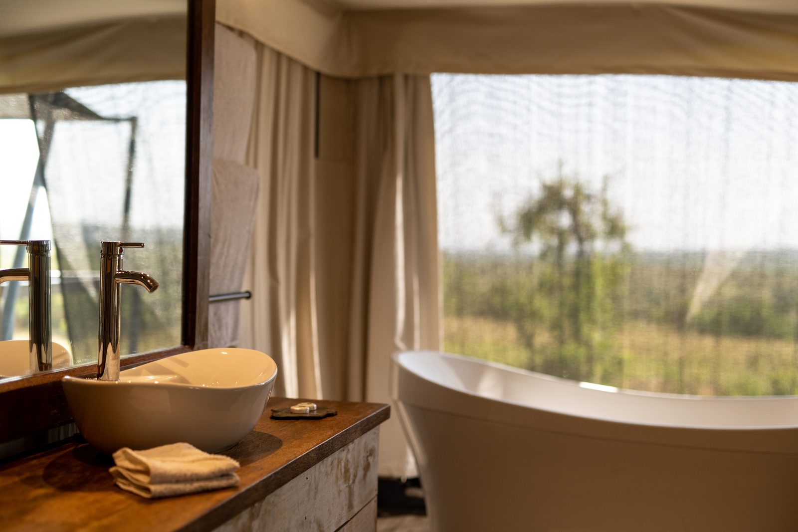 A modern bathroom featuring a sink and a freestanding bathtub, with a view of nature through a sheer curtain.