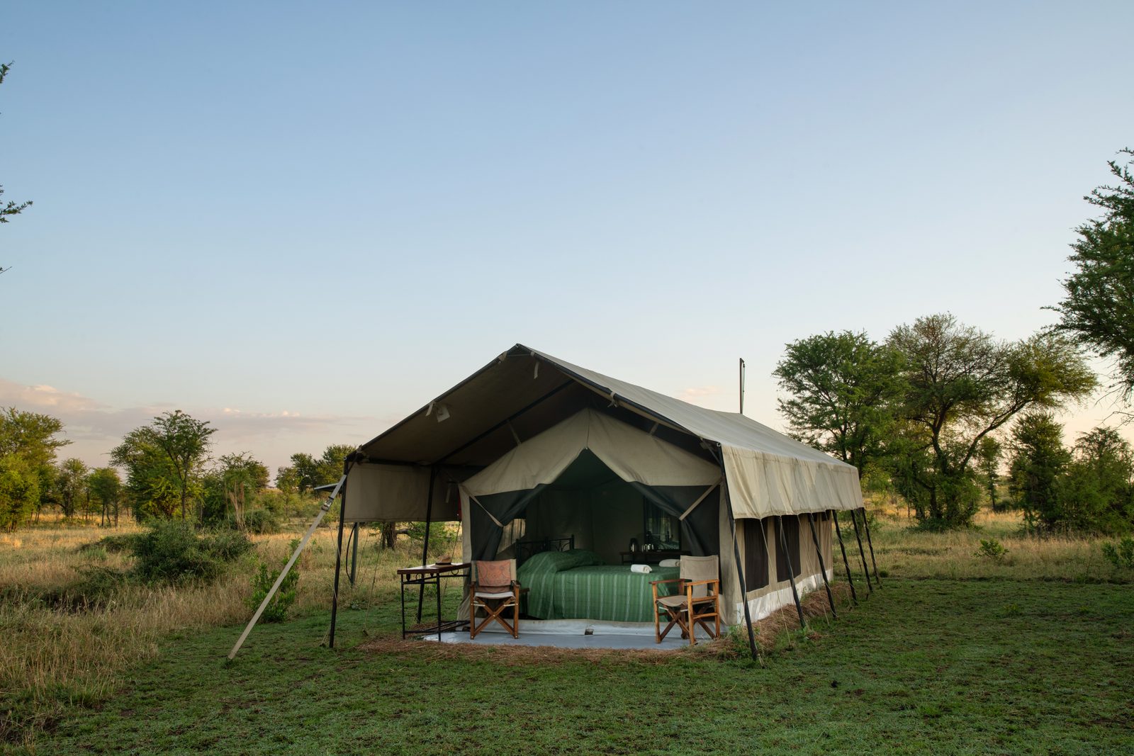 A safari tent set up in a grassy area surrounded by trees.
