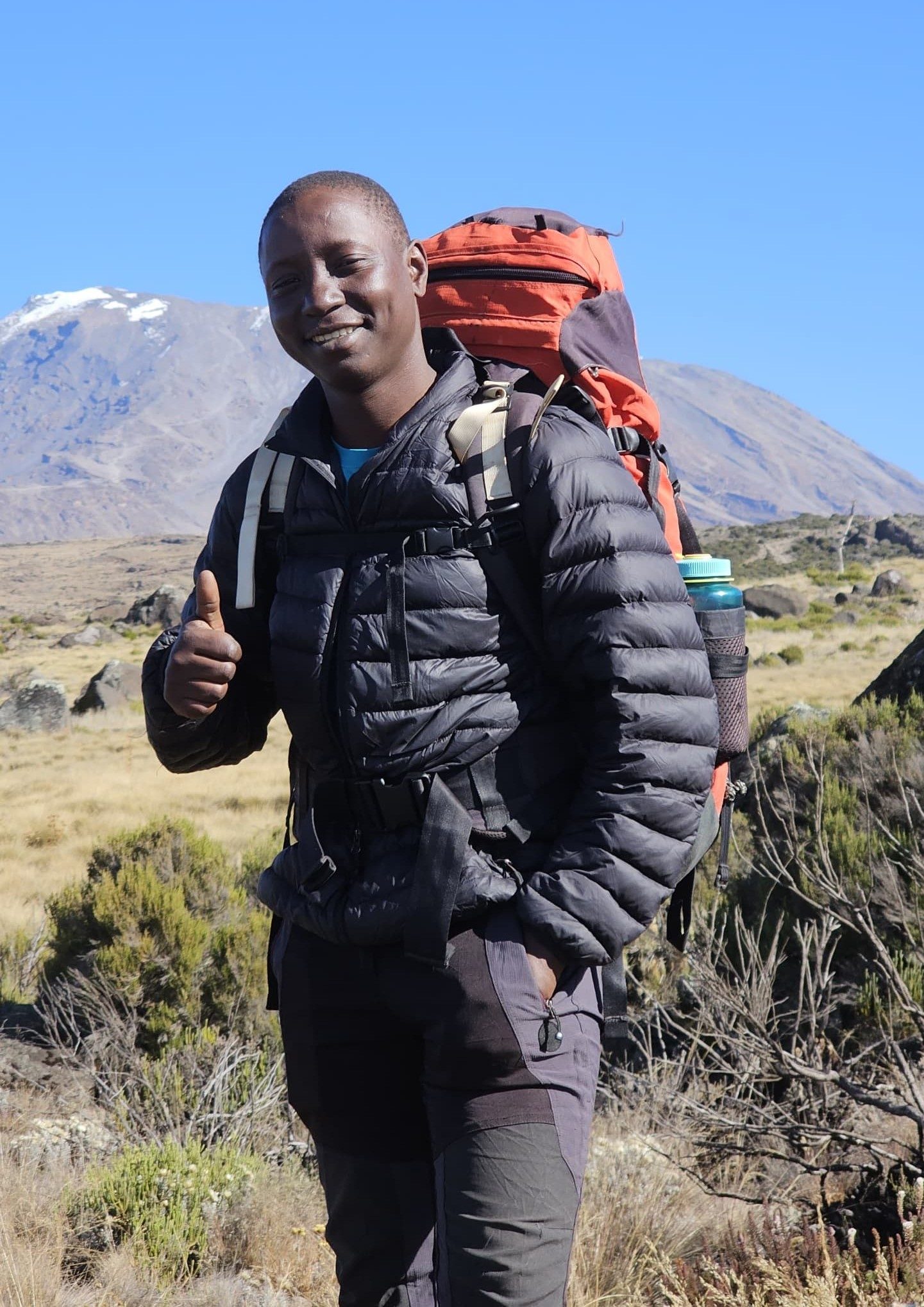 A person with a backpack giving a thumbs up in a mountainous landscape.