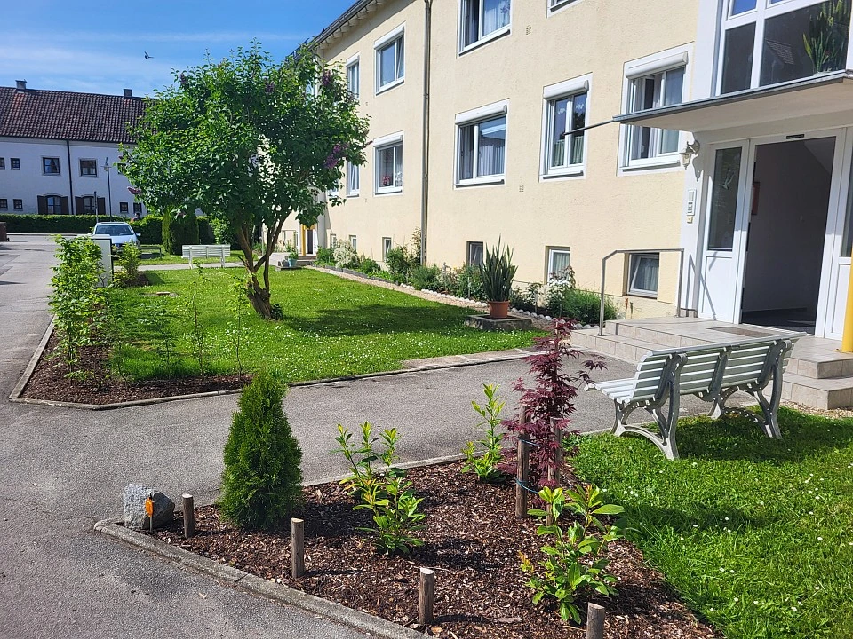 Liebevoll gestalteter Garten mit Rasenfläche, Beeten und Sitzbank vor dem Wohnhaus in der Salvatorstraße 2a